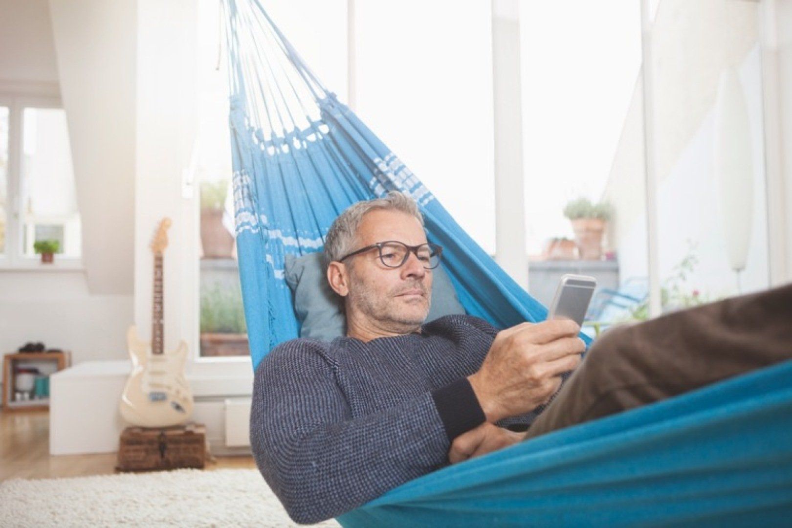 Mann Zuhause auf Haengematte mit Smartphone
