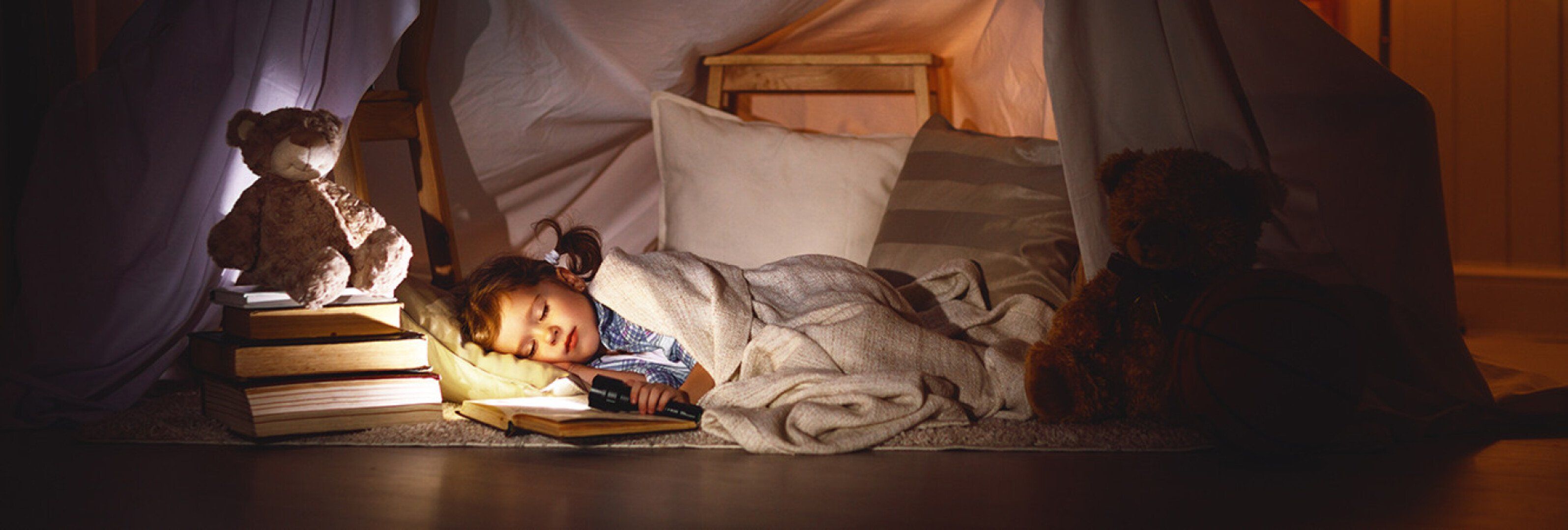 Kind liegt im Zelt mit Taschenlampe