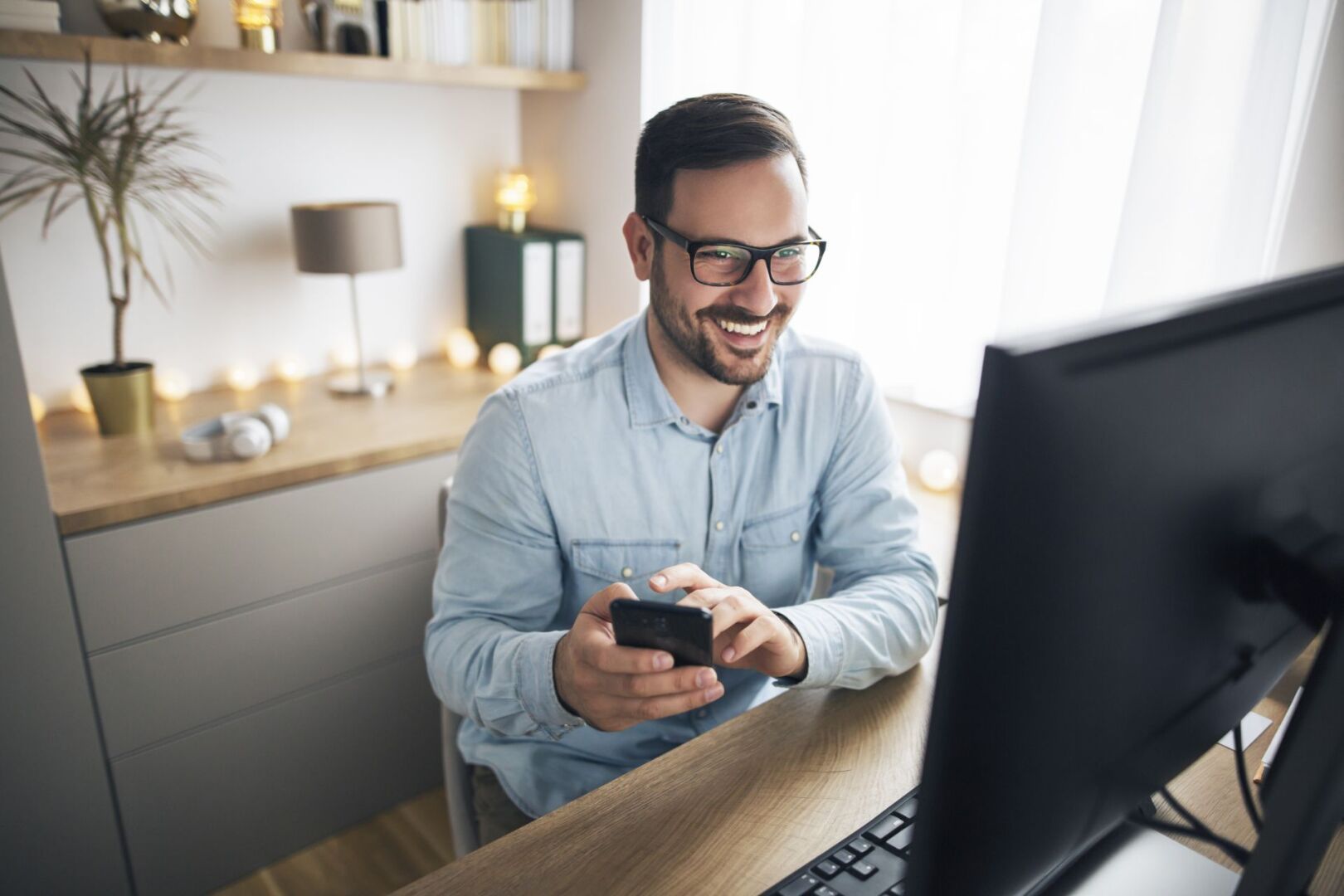 Es ist ein Mann zu sehen, der im Home Office an seinem Schreibtisch sitzt und sein Telefon in der Hand hält, um jemanden anzurufen.