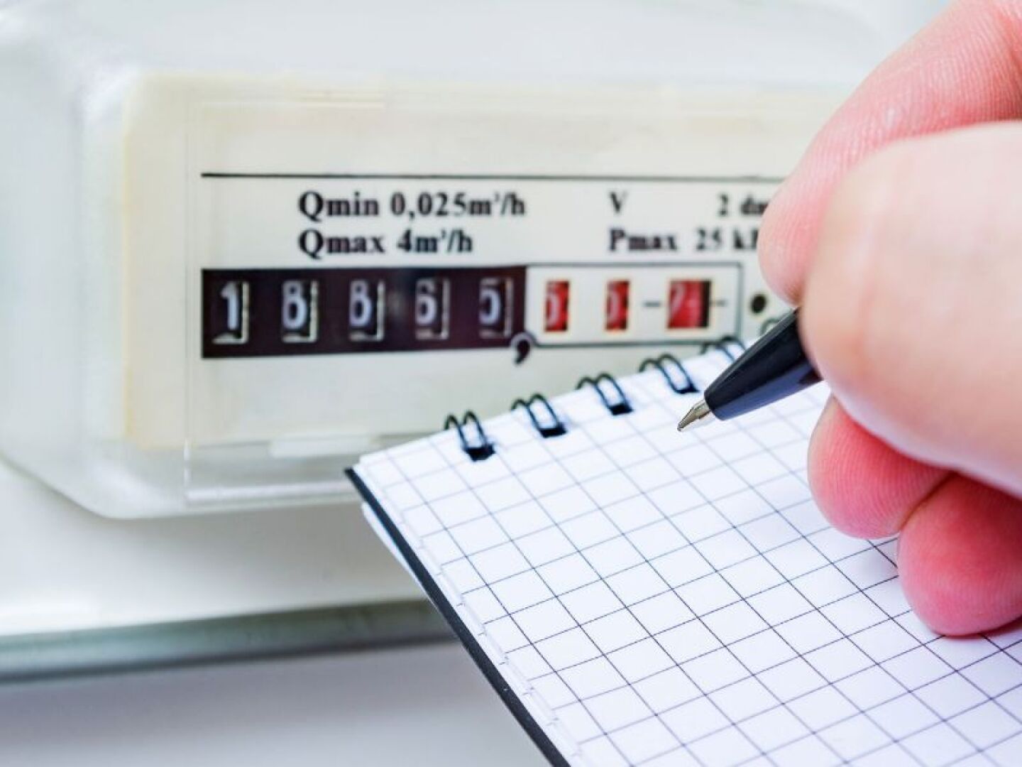 Zu sehen ist der Zählerstand einer Gasheizung, eine Hand notiert etwas auf einem Blatt.