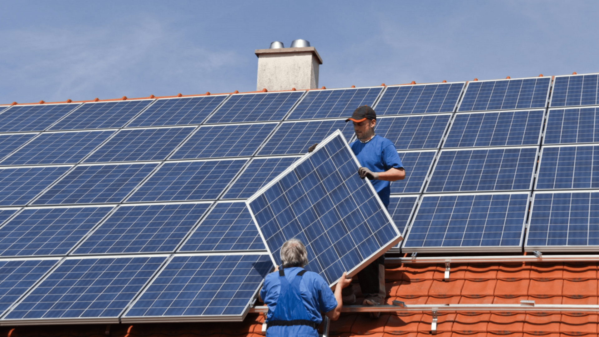 Zwei Handwerker installieren eine Photovoltaikanlage auf einem Dach, das alle Voraussetzungen erfüllt.