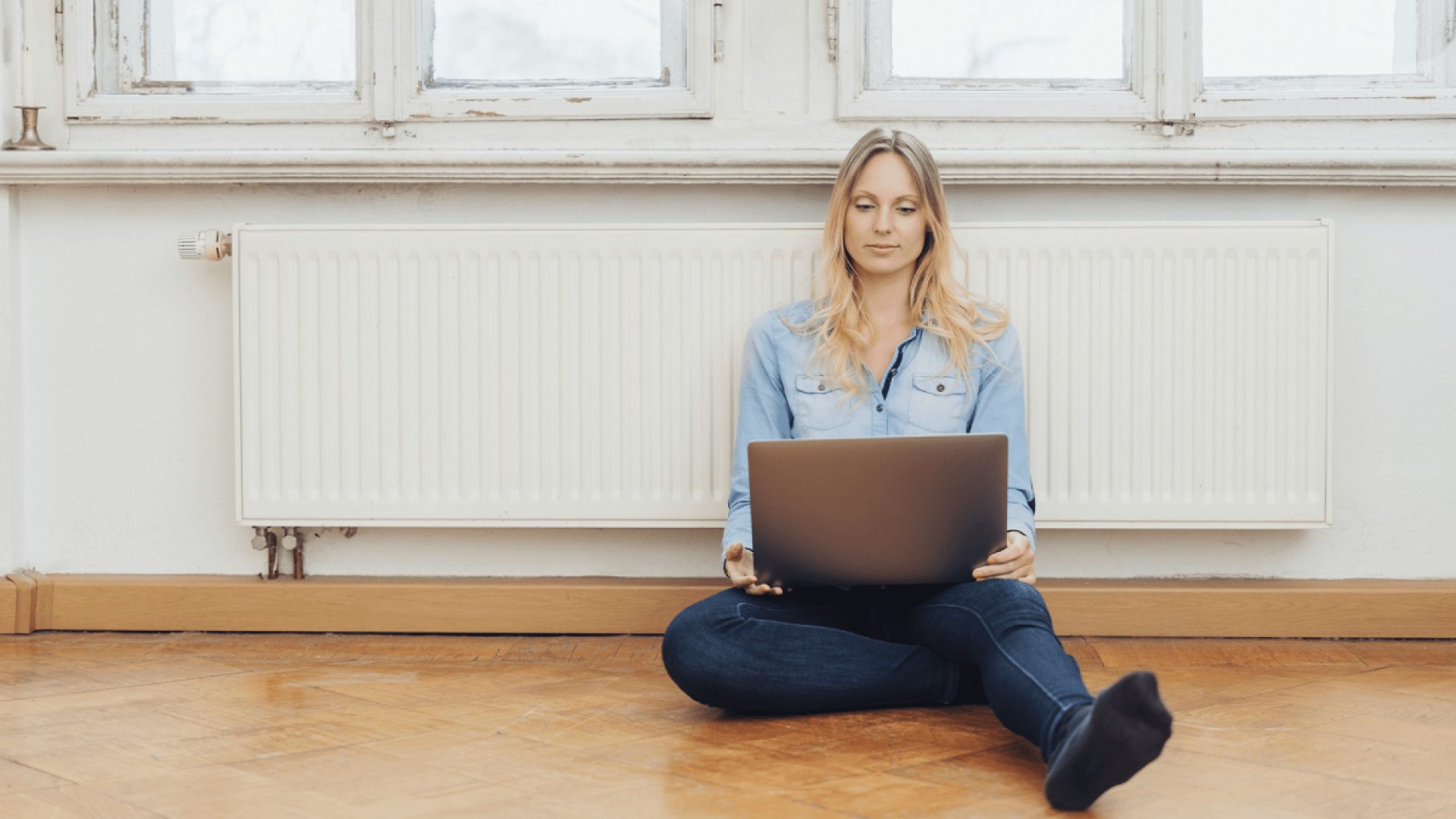 Eine Frau sitzt vor der Heizung und berechnet ihre Heizkosten.