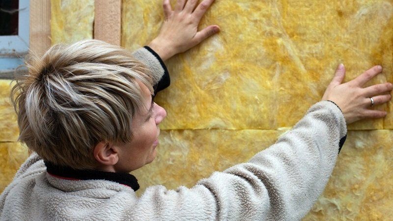 Eine Expertin bringt zum Sparen der Heizkosten eine Dämmung an einer Hauswand an.