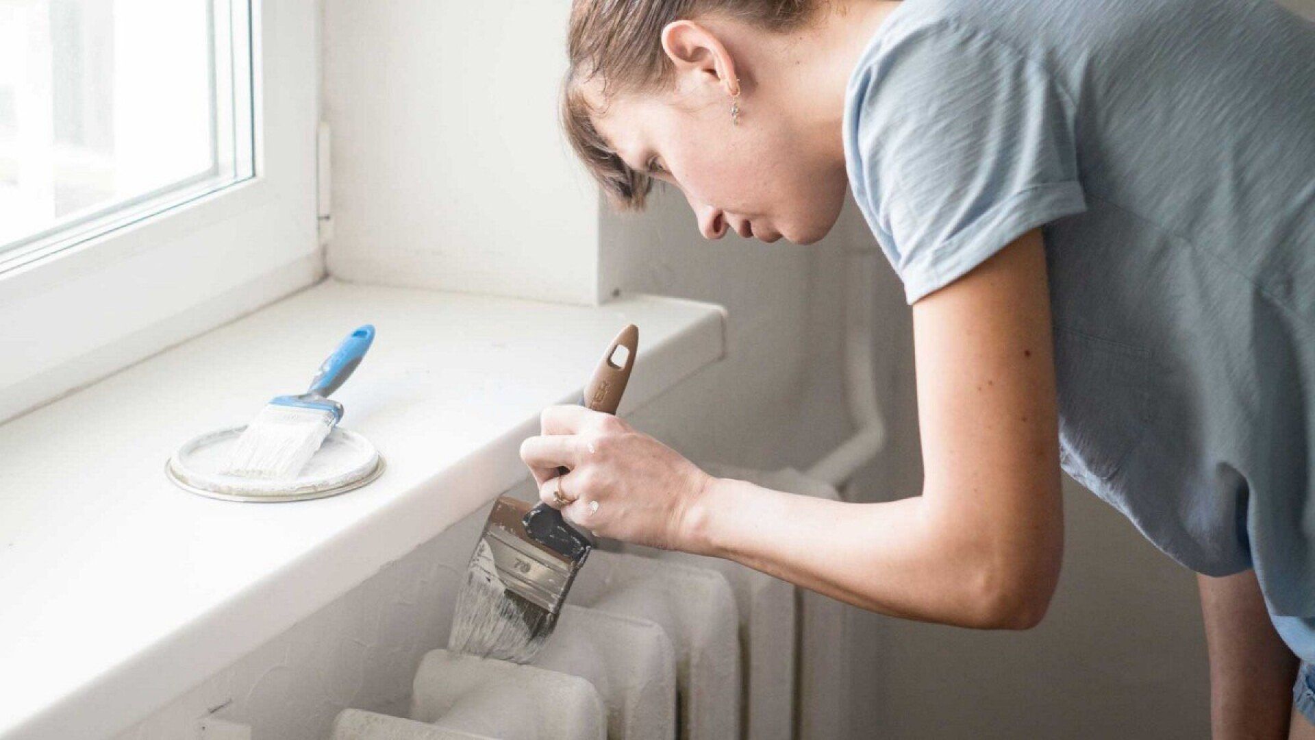 Eine Frau beginnt mit einem Pinsel den Heizkörper zu streichen.