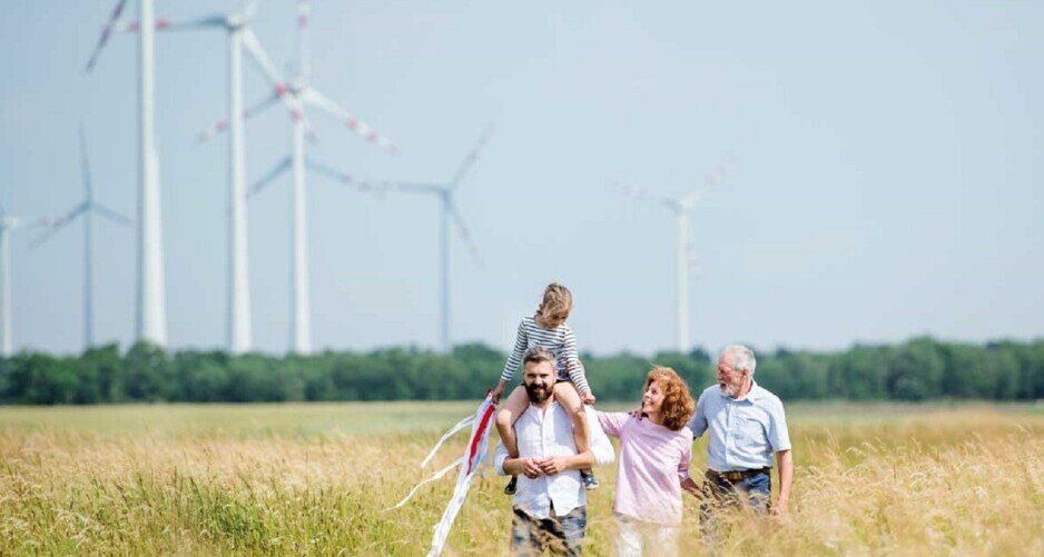 Eine Familie läuft über ein Feld mit Windrädern im Hintergrund, die Windenergie erzeugen.