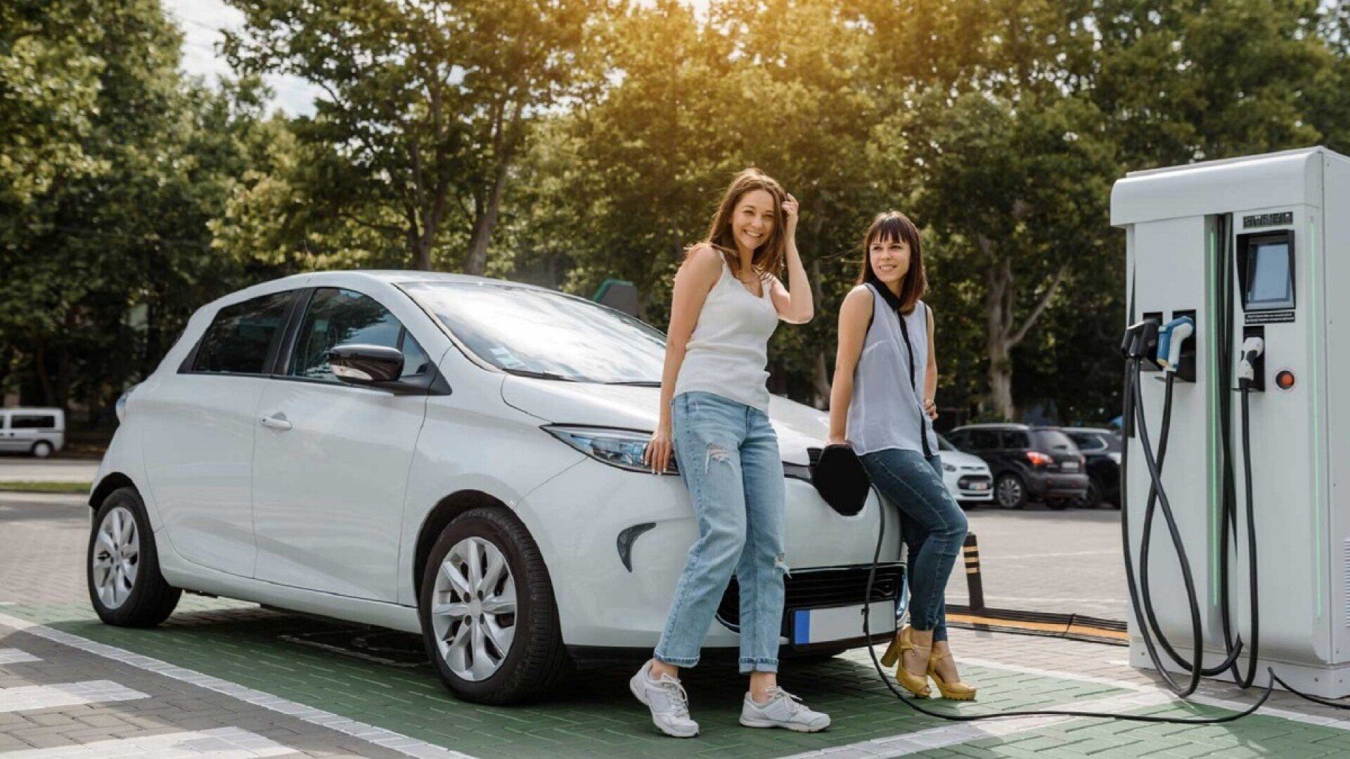 Zwei Frauen stehen an einer Ladestation mit ihrem E-Auto, die sie über die Routenplanung gefunden haben.