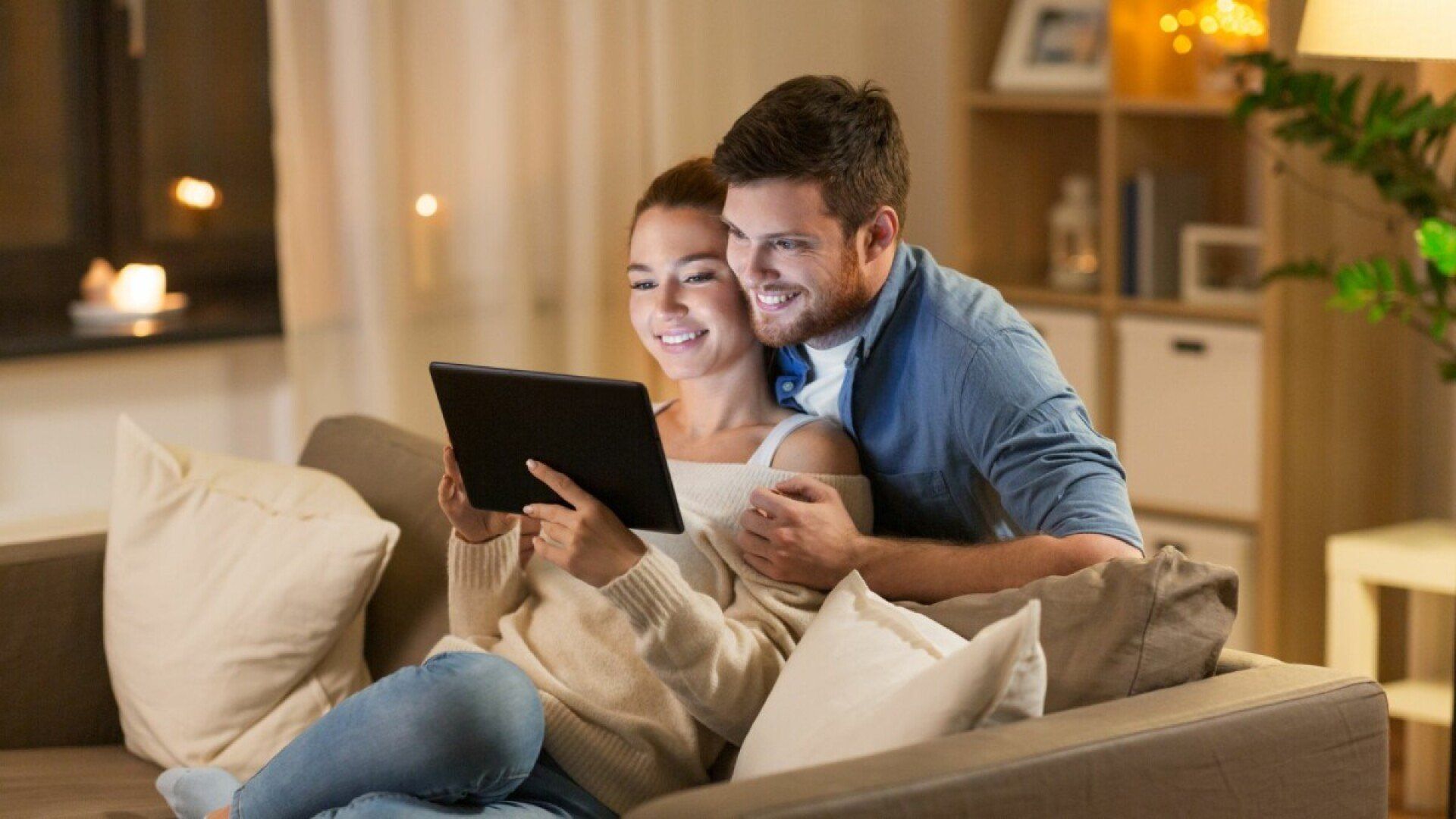 Ein Pärchen liegt auf der Couch und freut sich, weil es im Alltag Energie sparen kann.