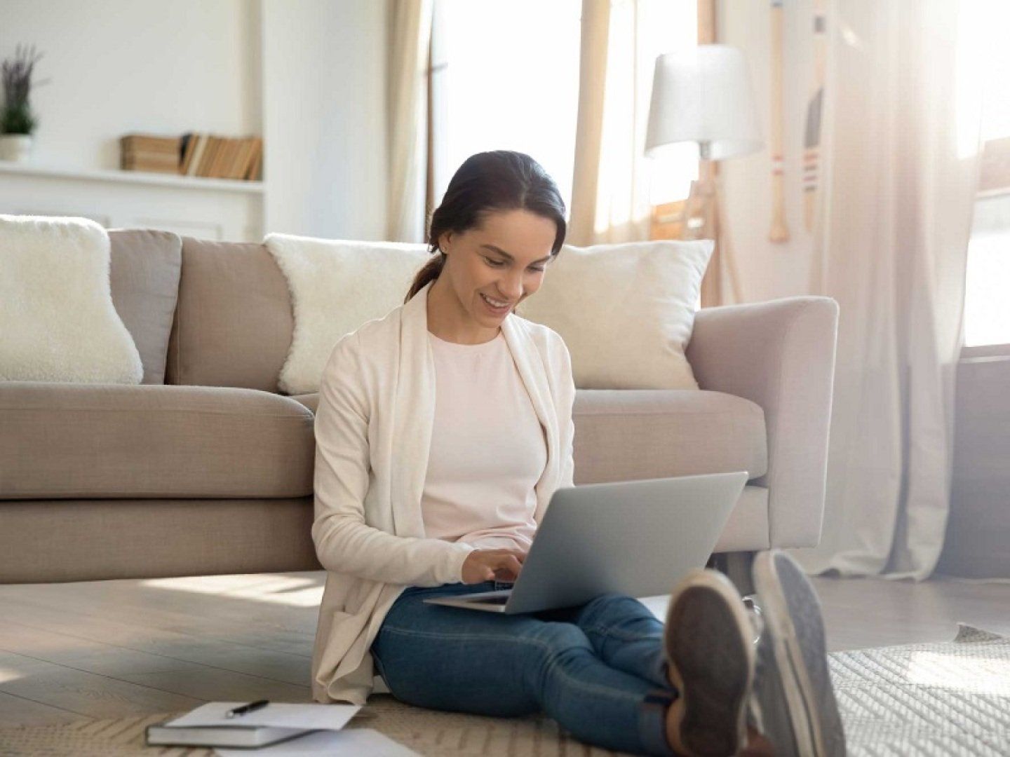 Eine Frau sitzt an ihrem Laptop auf dem Boden, möchte ihre Ölheizung erneuern und informiert sich über Alternativen wie Wärmepumpen.