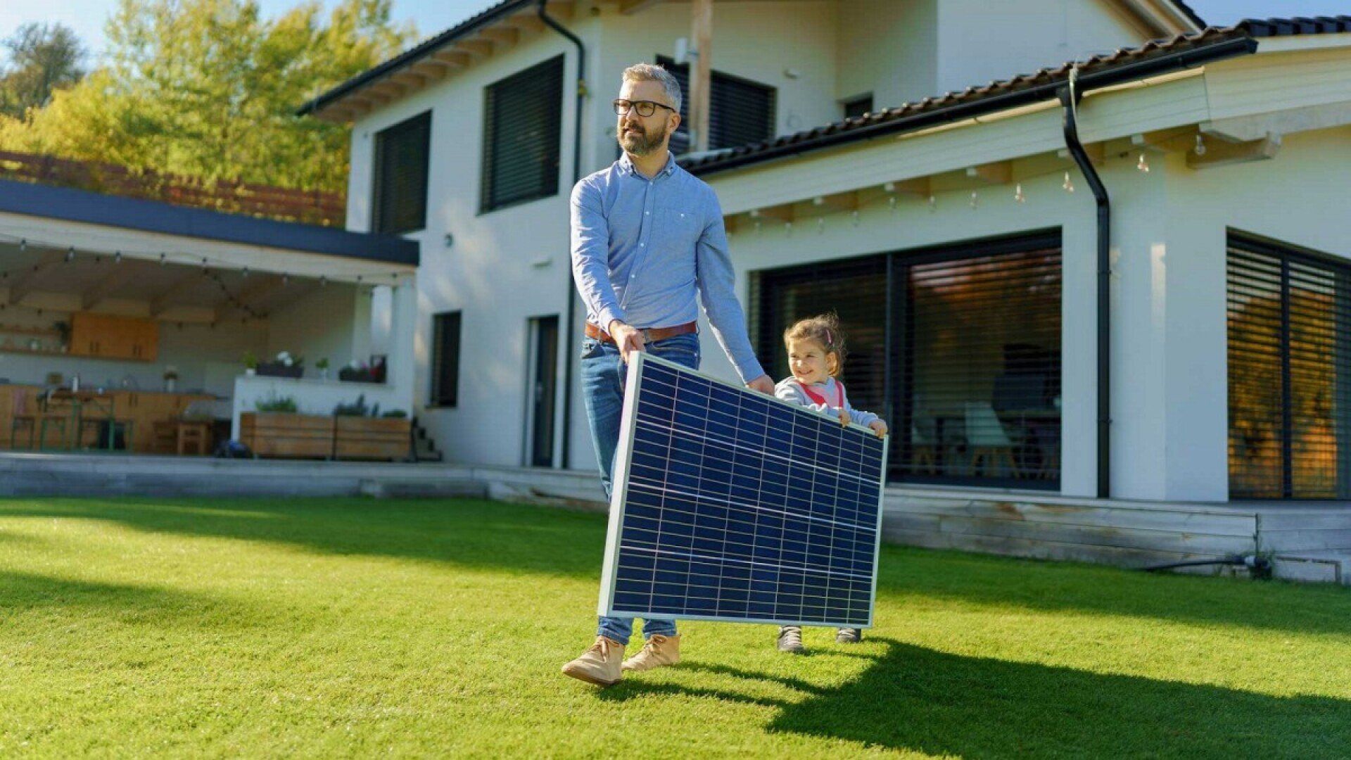 Ein Vater trägt mit seiner Tochter ein Solarpanel über die Wiese.