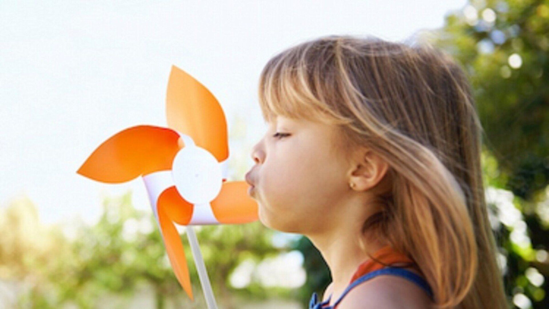 Ein Kind pustet ein Windrad an, das symbolisch für Ökostrom steht.
