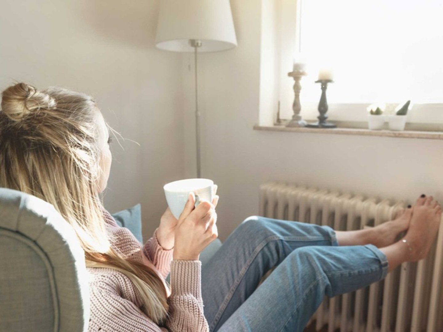 Eine Frau wärmt ihre Füße an einem Heizkörper, der dank einer Wärmepumpe warm ist.