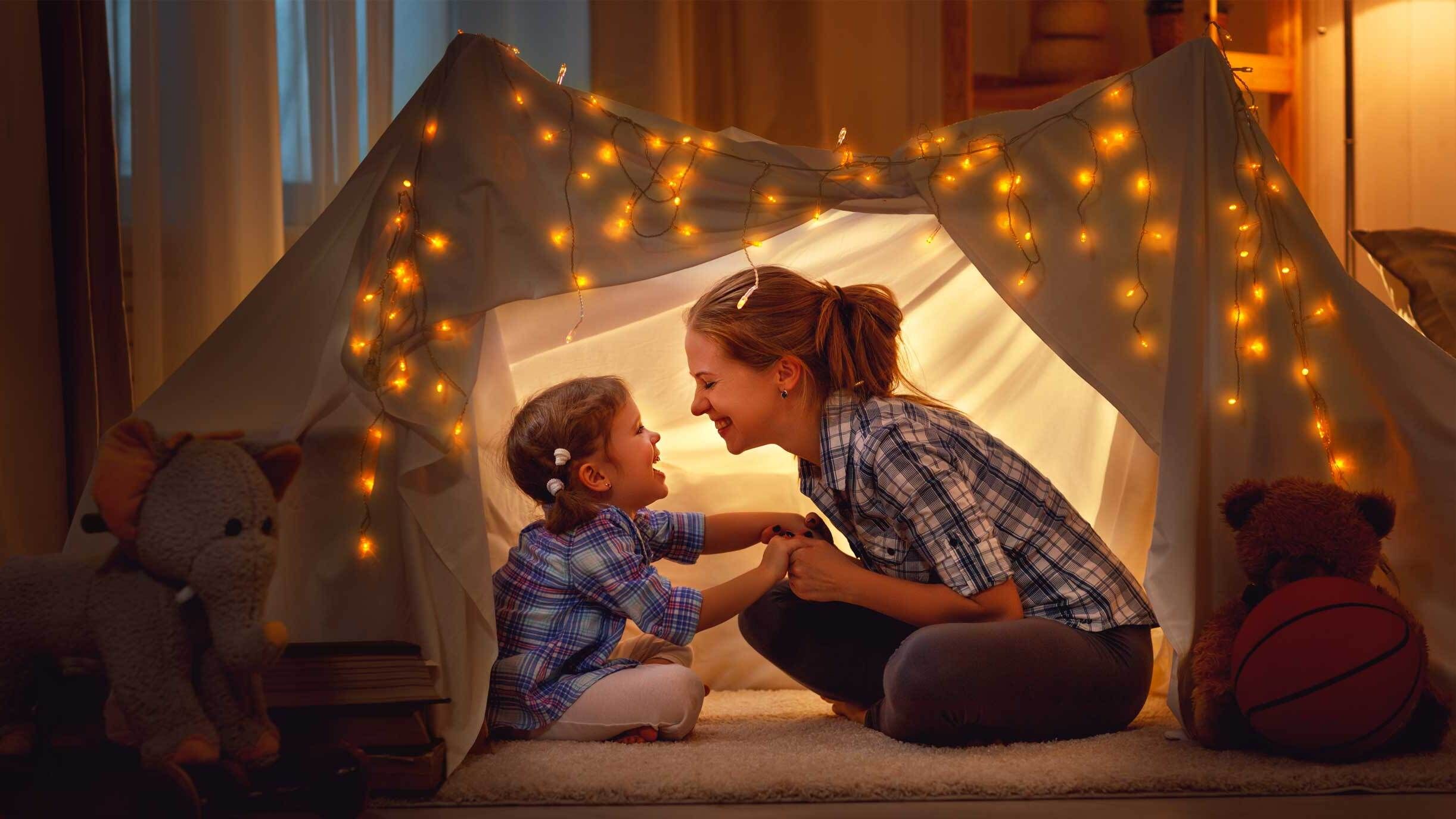 Eine Frau mit Kind in einem Zelt im Wohnzimmer bei gedämpftem Licht mit einer Lichterkette.