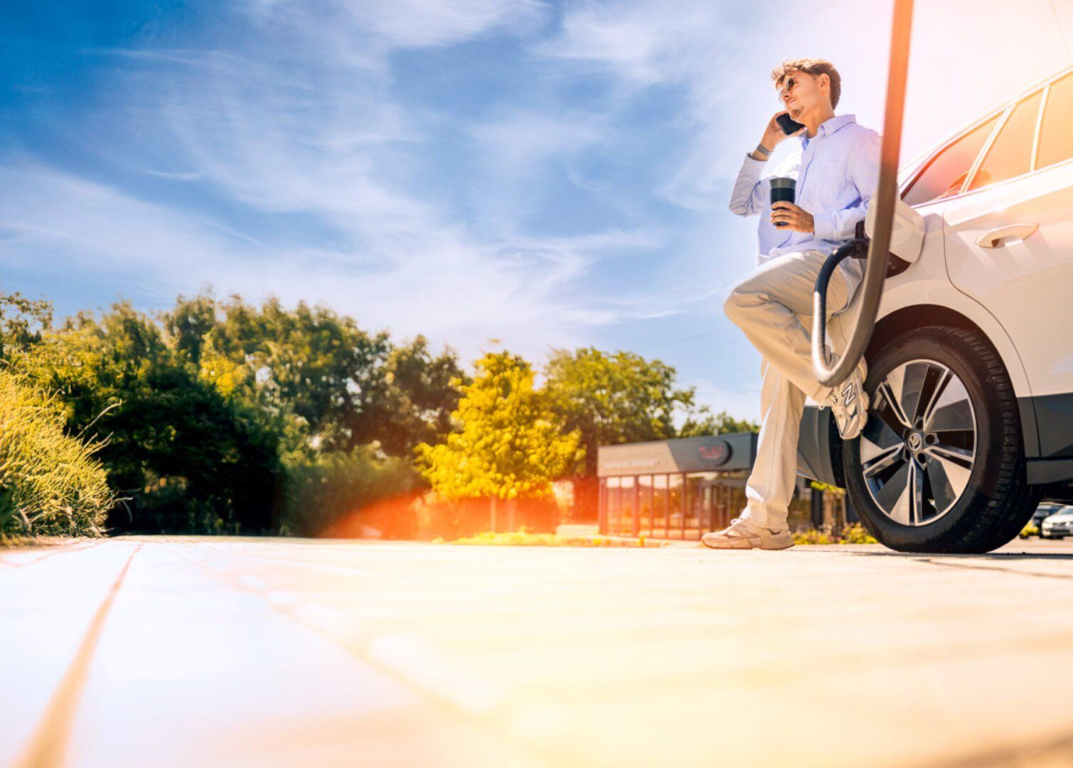 Junger Mann lehnt an E-Auto, das an Ladesäule hängt, und telefoniert