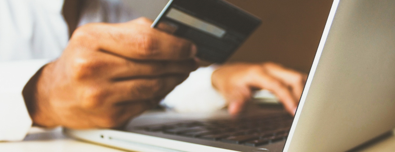 Zu sehen ist ein Mann, der seine Kreditkartendaten an einem Laptop eintippt und damit sicher online einkauft