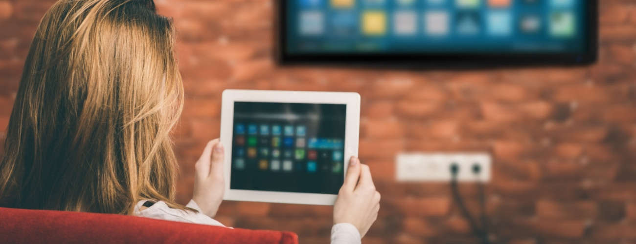 Eine Frau steuert einen Smart TV über ein Tablet