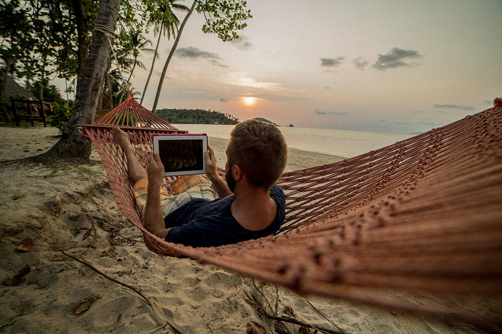 Mann am Strand schaut in Hängematte auf Smartphone