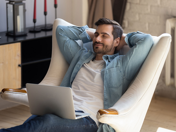 Das Bild zeigt einen Mann, der zufrieden vor einer Heizung sitzt, da er durch das richtige Einstellen des Thermostats Heizkosten spart. 