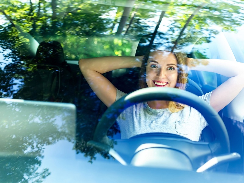 Eine Frau sitzt glücklich in ihrem Elektroauto, das sie gebraucht gekauft hat und durch die Förderung noch mehr Kosten gespart hat.